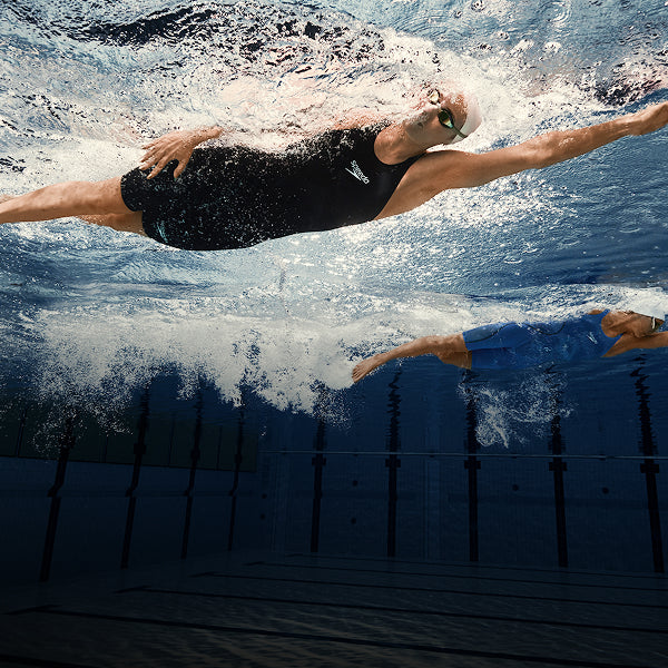 Swimmer gliding underwater in a pool with another swimmer behind.