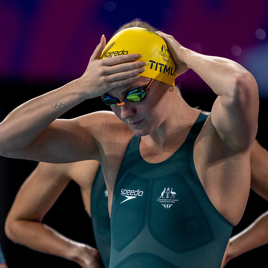 Swimmer in a cap and goggles adjusting her headgear before a race.