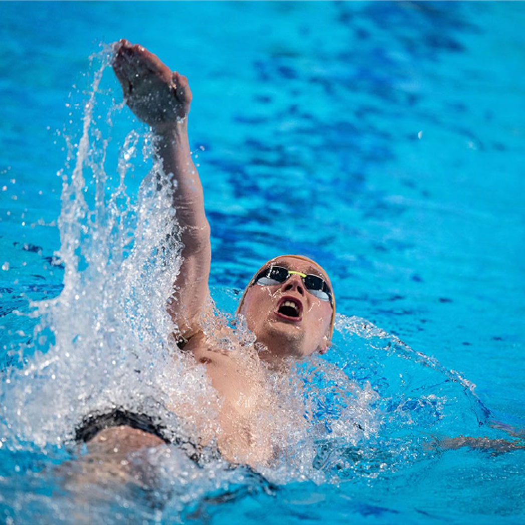 Swimmer doing backstroke in a pool, arm raised with water splashing.