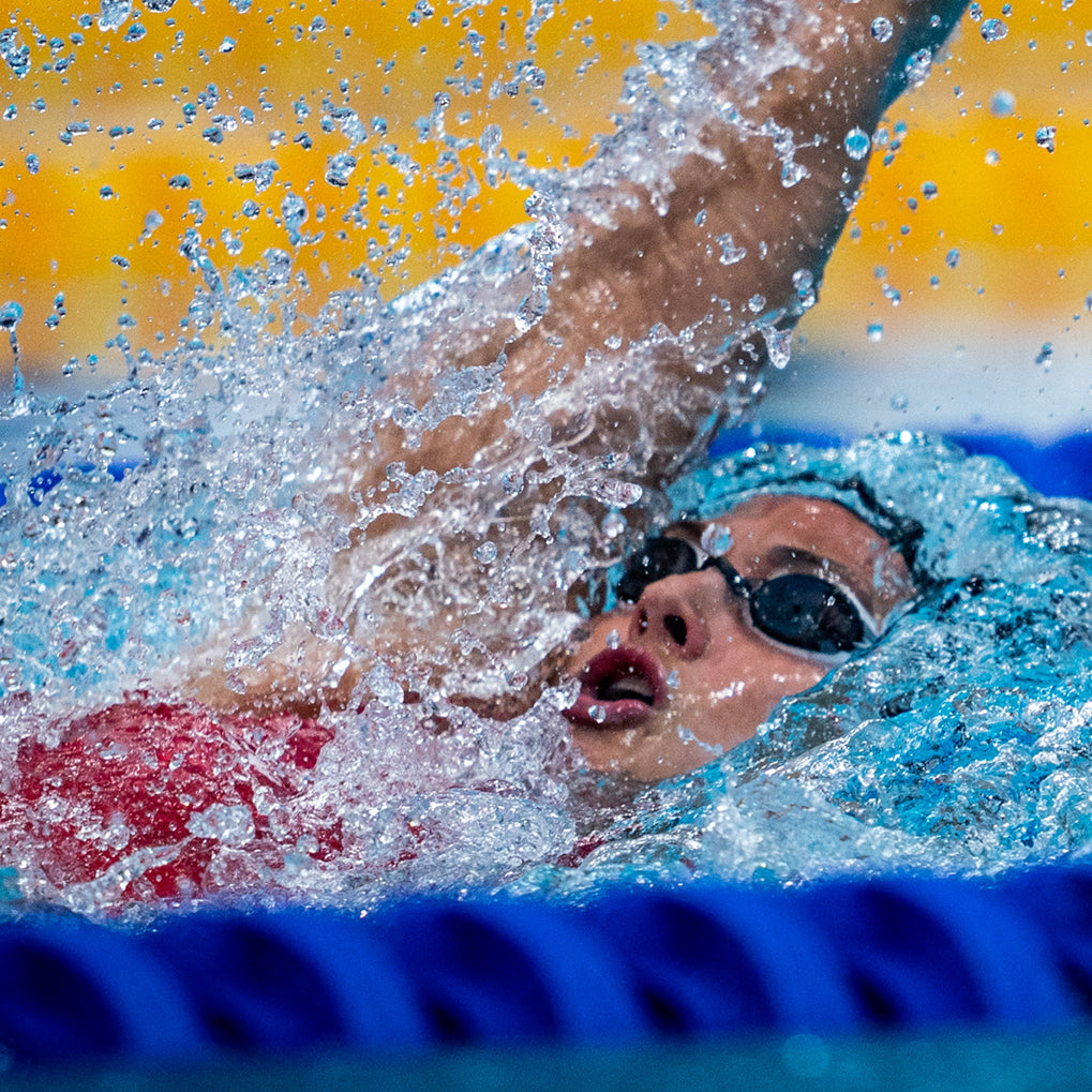 Swimmer mid-stroke in a pool, splashing water, wearing goggles.