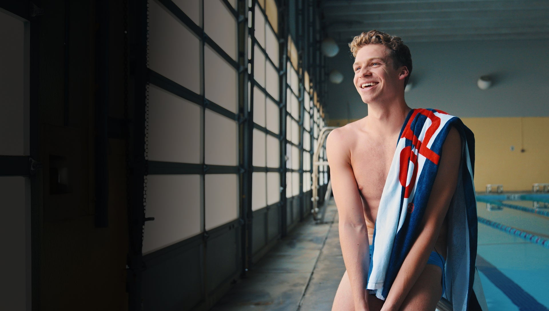 Smiling swimmer with a towel over his shoulder standing by the pool.