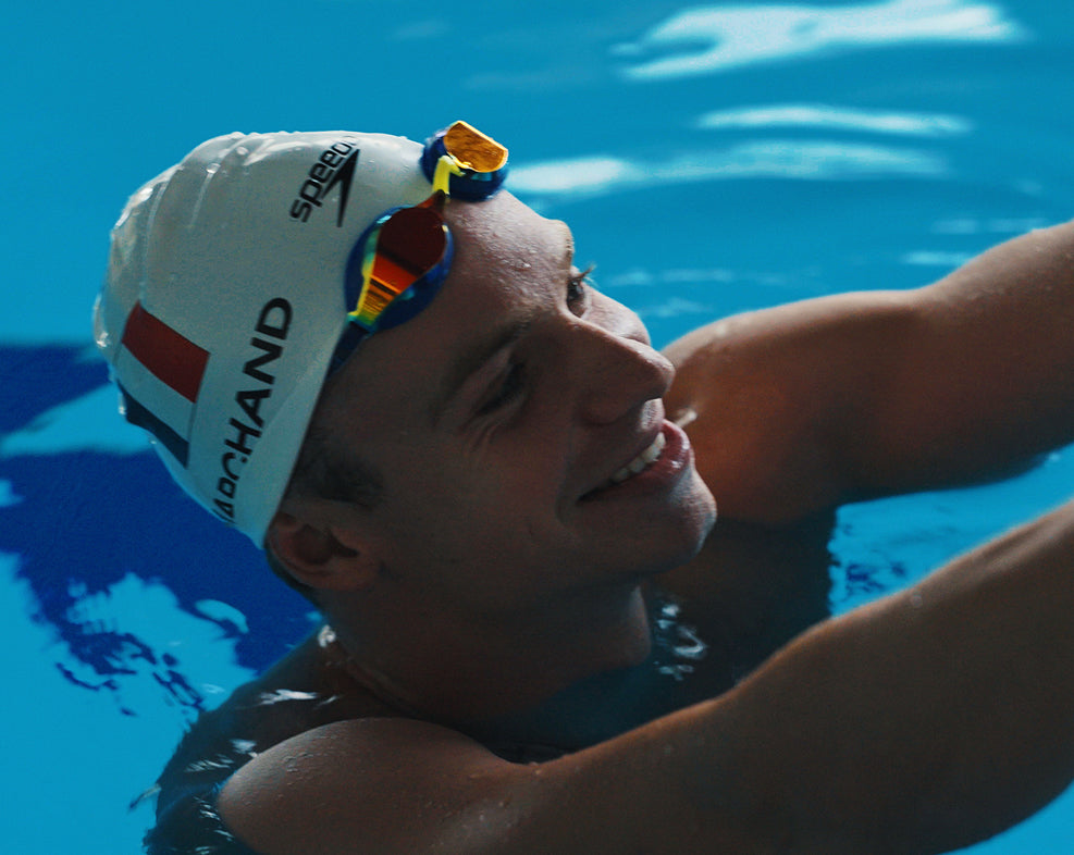 Smiling swimmer in a cap and goggles relaxing in the pool.